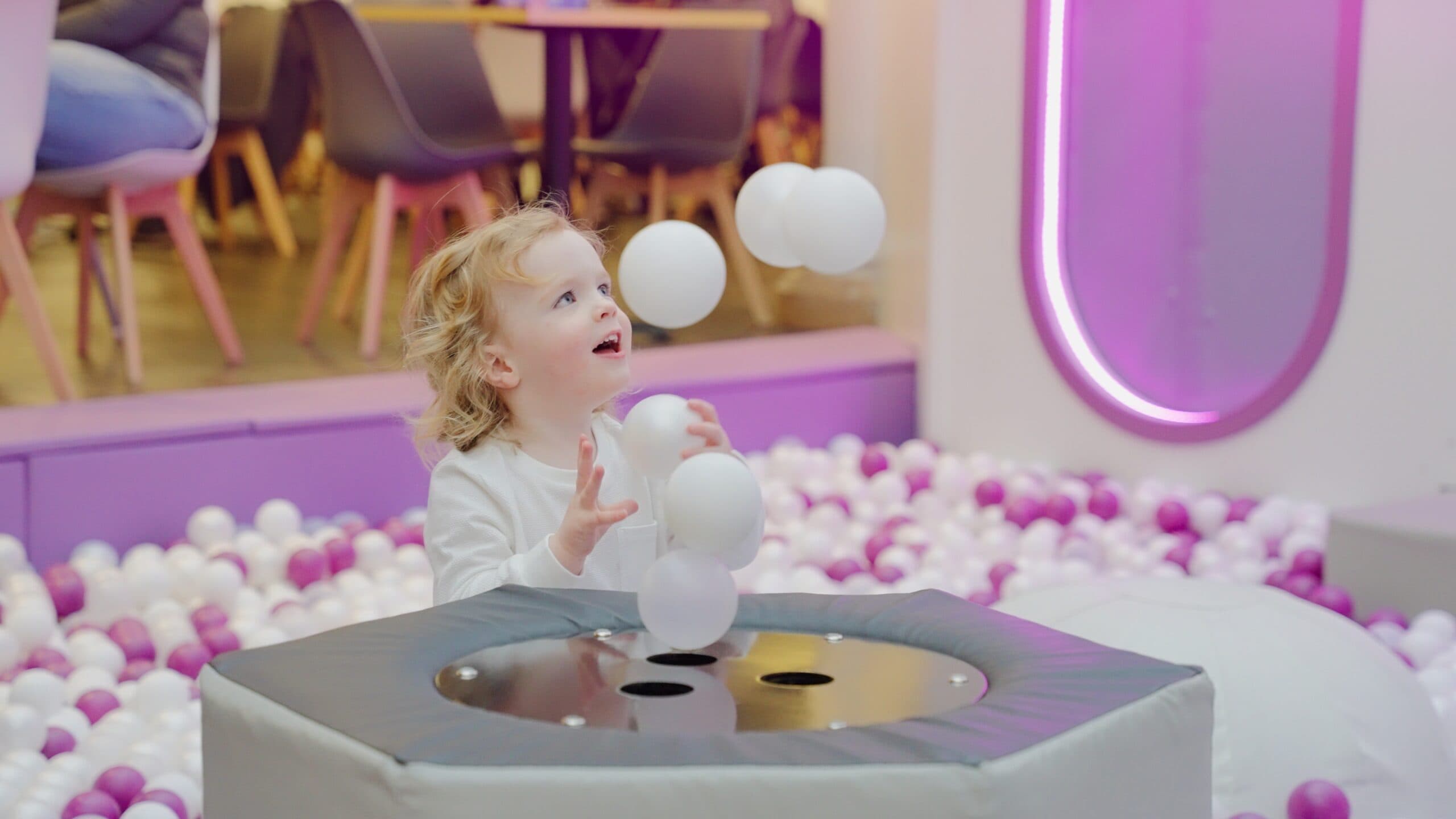 Toddler playing with balls at interactive sensory table in indoor play area